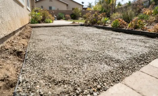 Professional artificial turf base preparation with compacted crushed rock foundation in an Inland Empire backyard