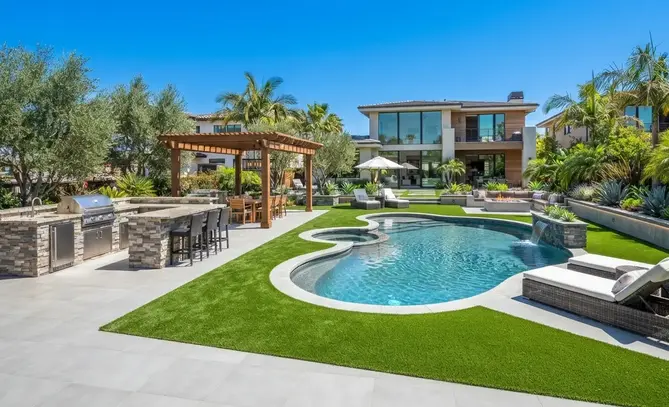 Luxury outdoor living space in the Inland Empire featuring poolside artificial turf connecting an outdoor kitchen, fire pit, pergola, lounge seating, walkways, and a modern swimming pool